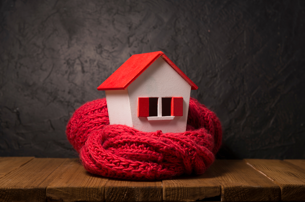 A small model of a house with red and white paint wrapped in a scarf on a wood surface.