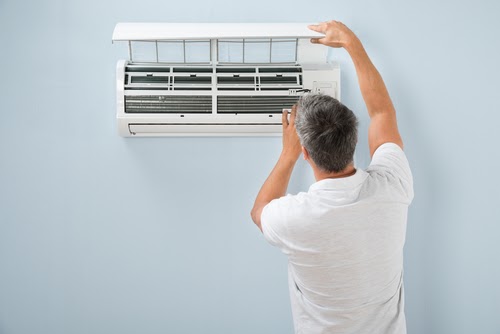 A man inspecting an indoor AC unit.