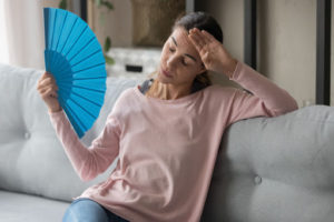 A woman sitting on a couch with a blue fan in her hand.