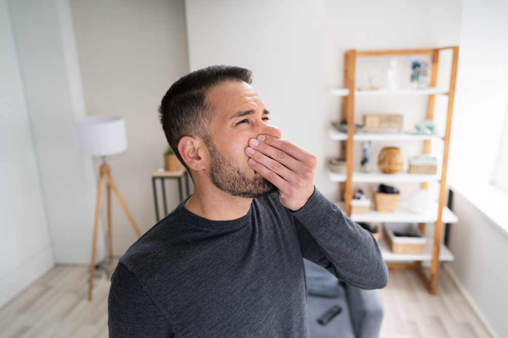 Man holding nose in his living room because furnace leaking gas stinks up his house