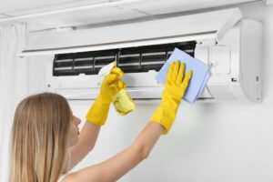 Woman wearing yellow cleaning gloves sprays and wipes down indoor AC unit