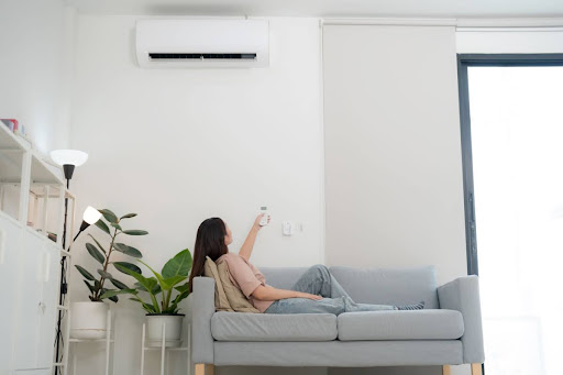Woman sitting on the couch in the living room using remote to adjust indoor AC unit.